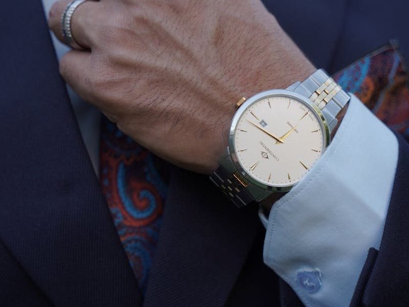 Close-up of a businessman adjusting a tie while showcasing an elegant wristwatch and suited style.