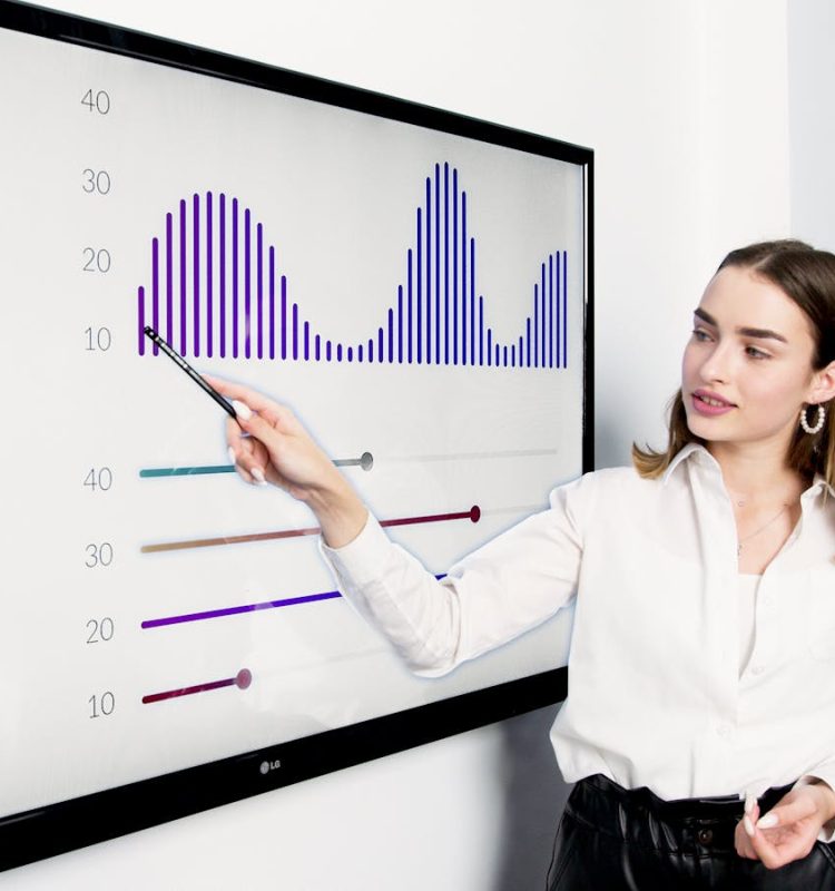 Businesswoman presenting data on a large digital screen in a modern office setting.